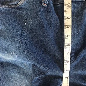 May include: Close-up of blue denim jeans with a measuring tape showing 12 inches. The jeans have a few small holes and are faded.