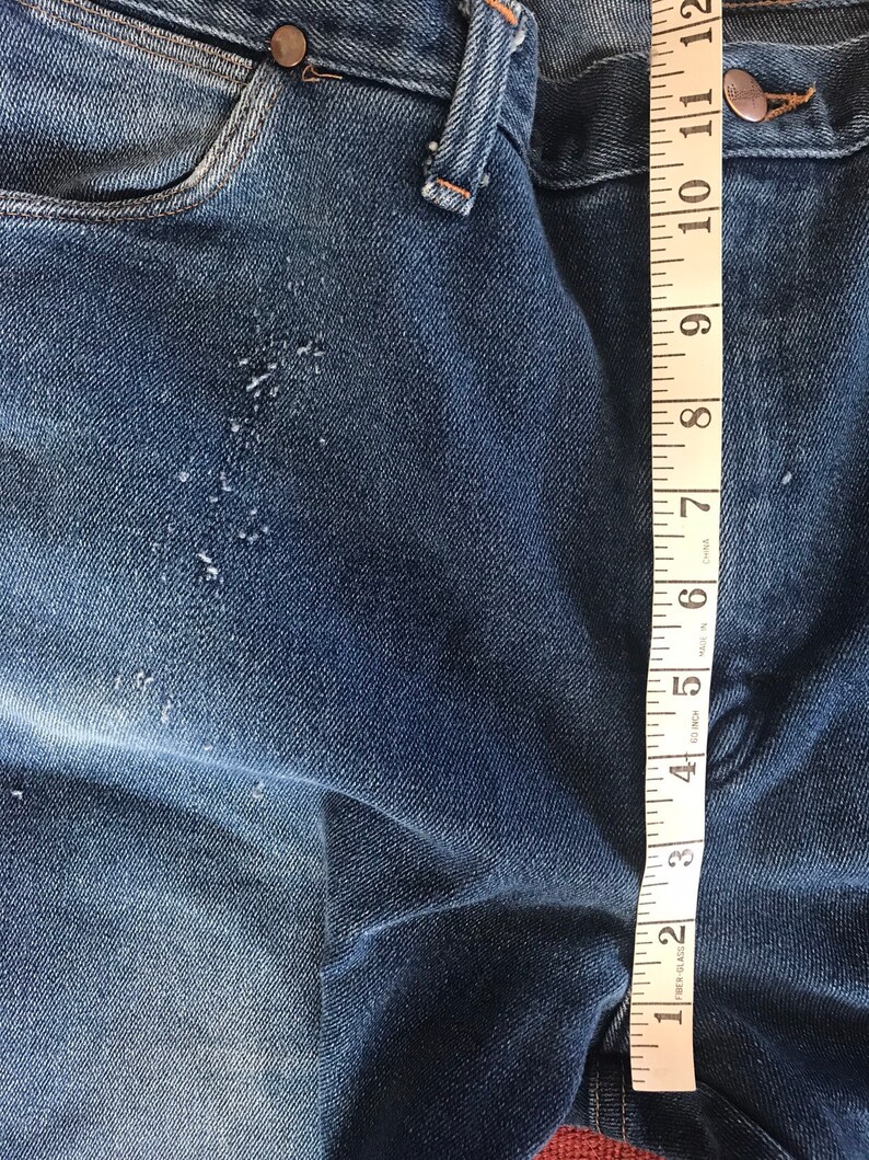 May include: Close-up of blue denim jeans with a measuring tape showing 12 inches. The jeans have a few small holes and are faded.