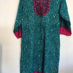 Puede incluir: Una t&uacute;nica azul turquesa con estampado floral rosa y blanco. El escote presenta un dise&ntilde;o bordado rosa y plateado con detalles de espejo. La t&uacute;nica tiene mangas tres cuartos y un ribete rosa alrededor del escote y el dobladillo.