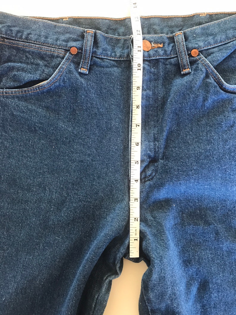 May include: A pair of blue denim jeans with a measuring tape placed along the center seam. The tape measures 12 inches.
