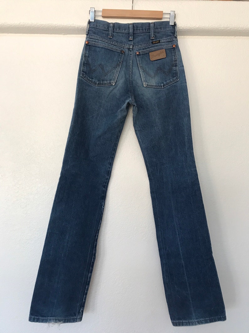 May include: A pair of blue denim jeans with a brown leather patch on the back pocket that says "Wrangler".