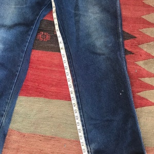 May include: A pair of dark blue denim jeans with a white measuring tape along the inseam. The tape measures 28 inches.