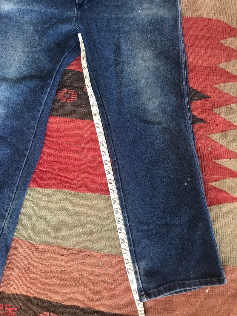 May include: A pair of dark blue denim jeans with a white measuring tape along the inseam. The tape measures 28 inches.
