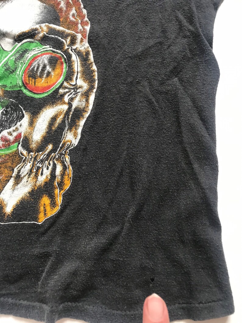 May include: Black t-shirt with a graphic print of a skull wearing green goggles. The skull has a white and orange design.