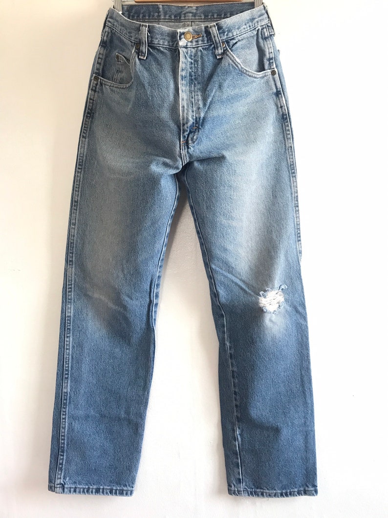 Pu&ograve; includere: Jeans in denim blu chiaro con un ginocchio consumato e una gamba dritta.