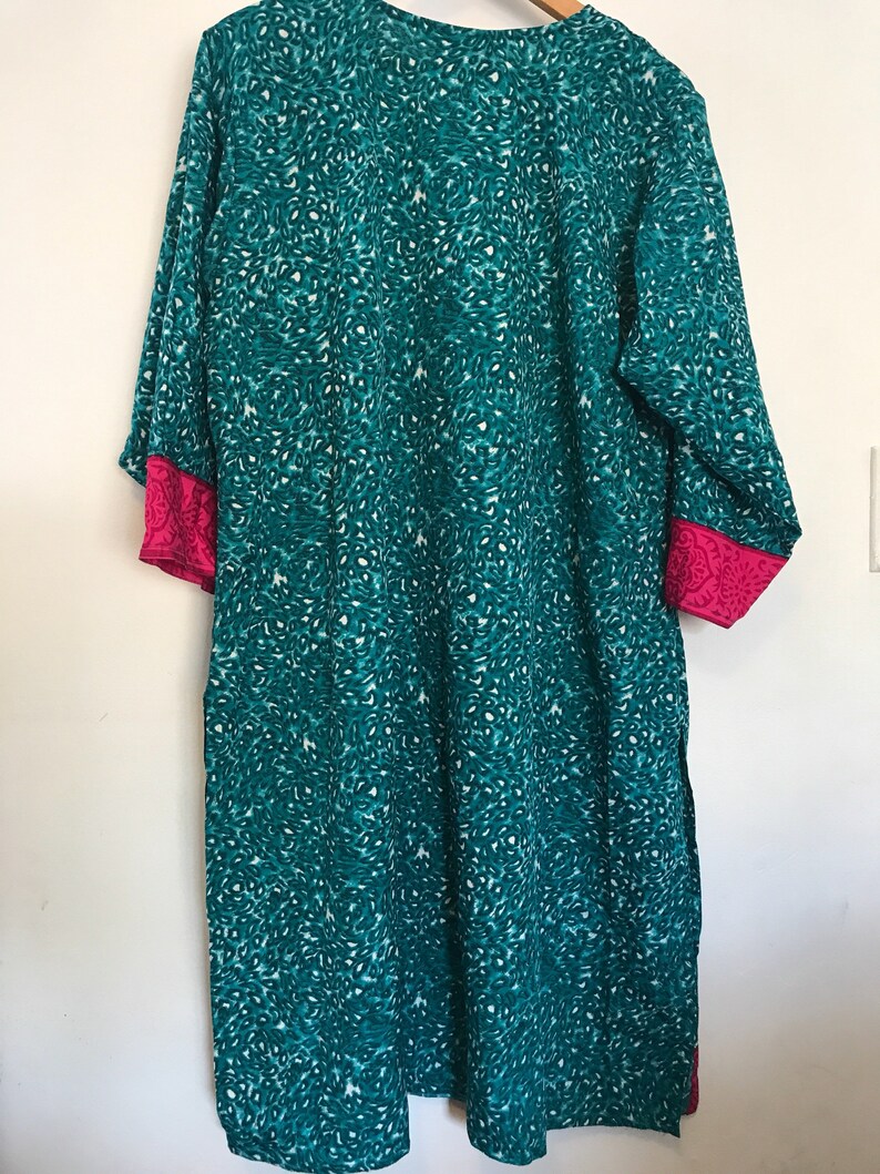Puede incluir: T&uacute;nica azul turquesa con estampado de leopardo blanco y turquesa. La t&uacute;nica tiene ribetes rosas en las mangas y una peque&ntilde;a abertura en la parte inferior.