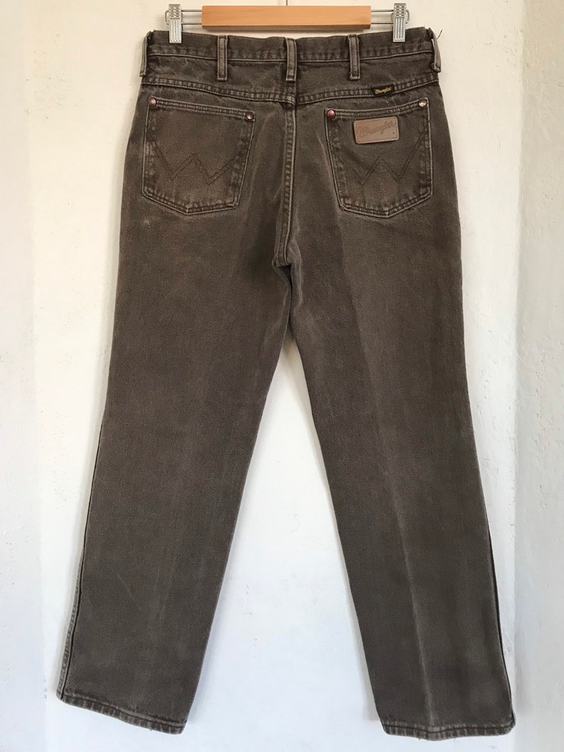May include: A pair of brown denim jeans with a leather patch on the back pocket that says "Wrangler".