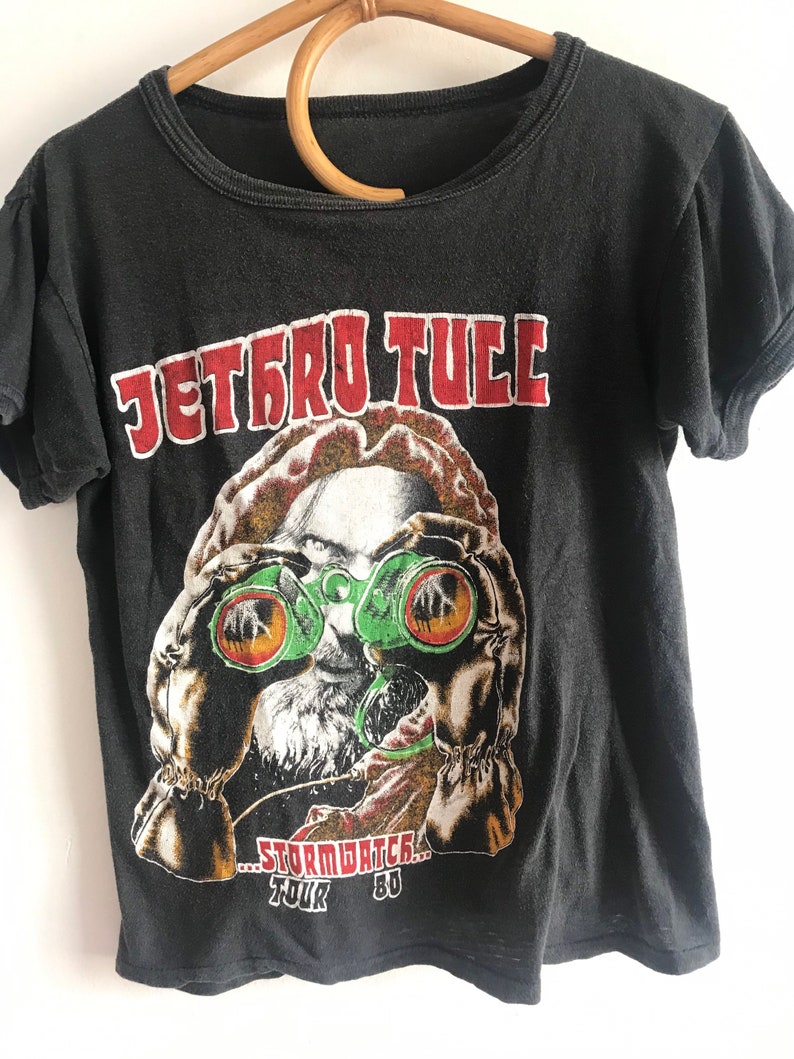 May include: Black t-shirt with a vintage Jethro Tull "Stormwatch" tour graphic. The graphic features a man wearing binoculars and a red, white, and blue hat.
