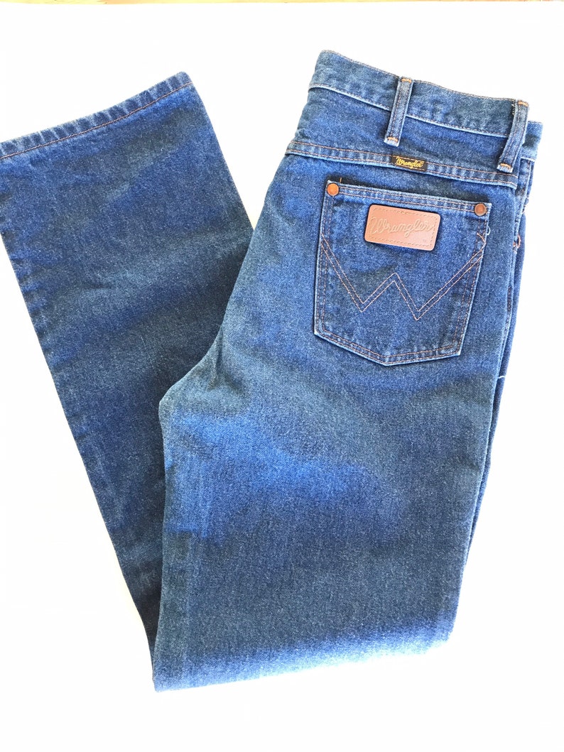 May include: A pair of blue denim jeans with a brown leather patch on the back pocket that says "Wrangler".