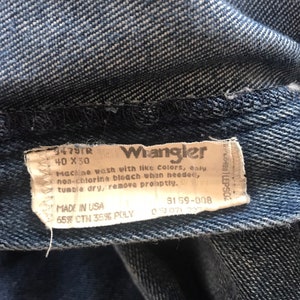 May include: A blue denim Wrangler jeans label with white text. The label says "9479TR 40 X 30 Wrangler Machine wash with like colors, only non-chlorine bleach when needed, tumble dry, remove promptly. MADE IN USA 3159-008 65% CTN 35% POLY".