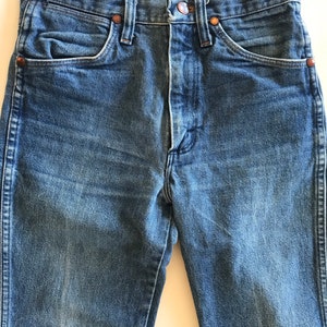 May include: A pair of blue denim jeans with a button fly and five pockets. The jeans are a classic style and have a faded look.