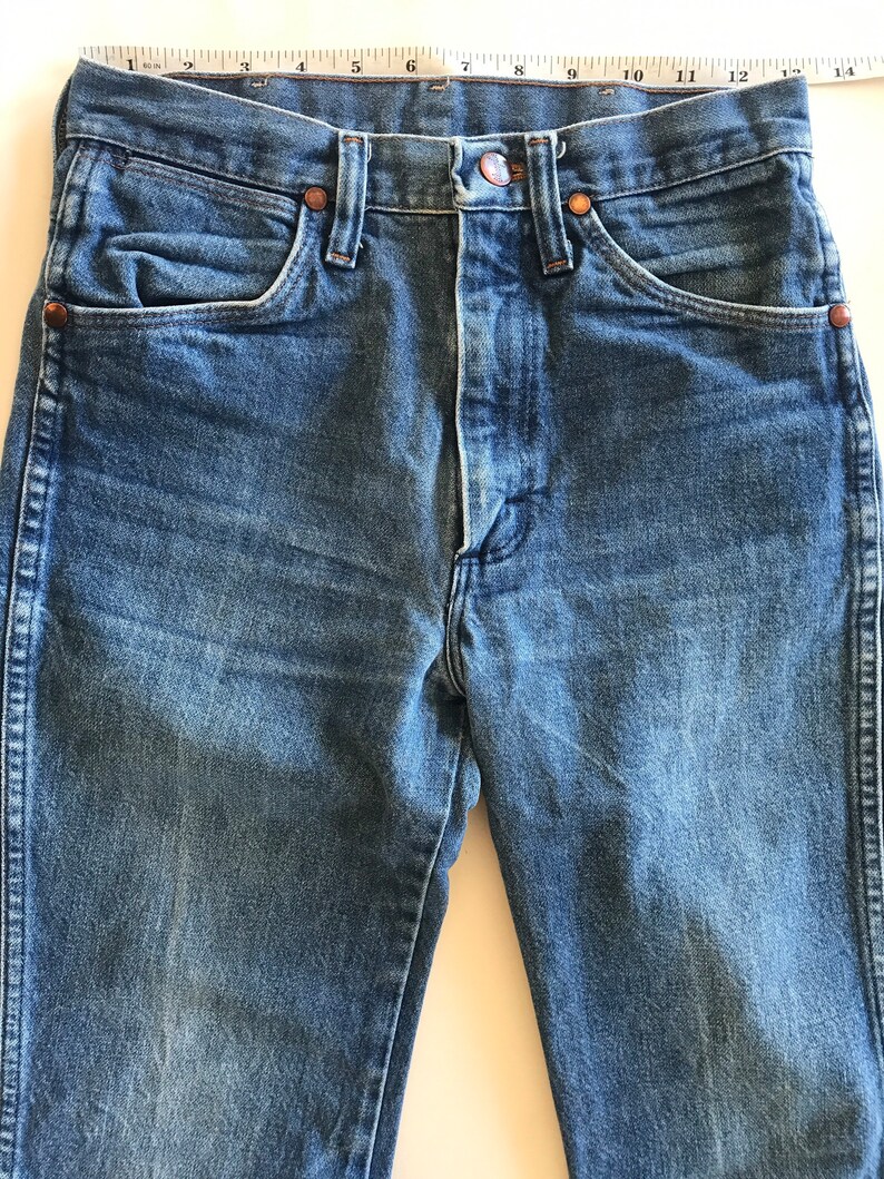 May include: A pair of blue denim jeans with a button fly and five pockets. The jeans are a classic style and have a faded look.