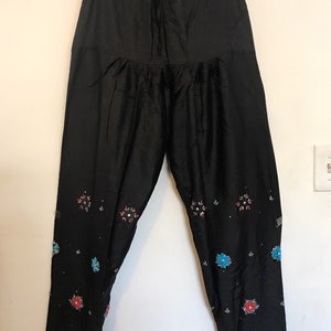 May include: Black pants with a drawstring waist and embroidered floral designs in shades of red, blue, and green.
