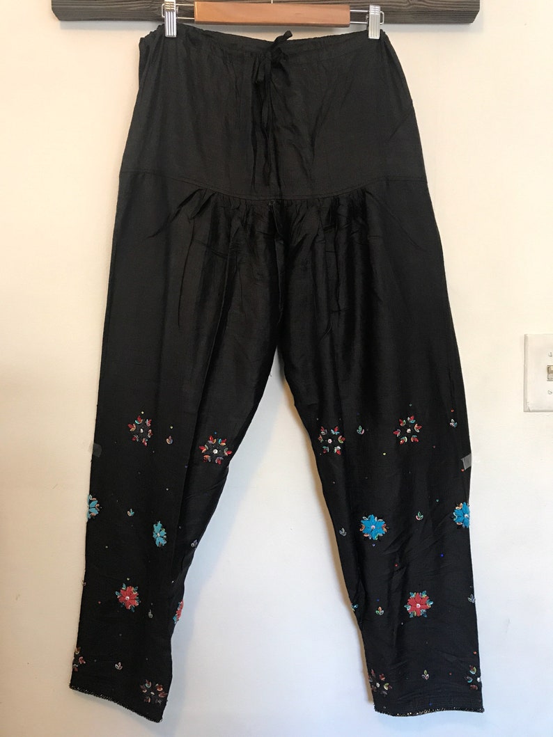 May include: Black pants with a drawstring waist and embroidered floral designs in shades of red, blue, and green.