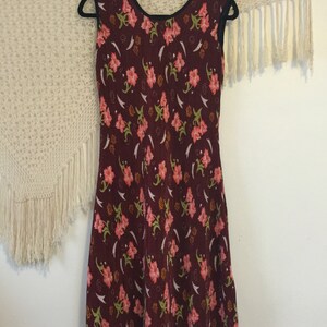 May include: A sleeveless burgundy dress with a floral print. The dress has a round neckline and a fitted bodice. The skirt is slightly flared and falls to the knees.