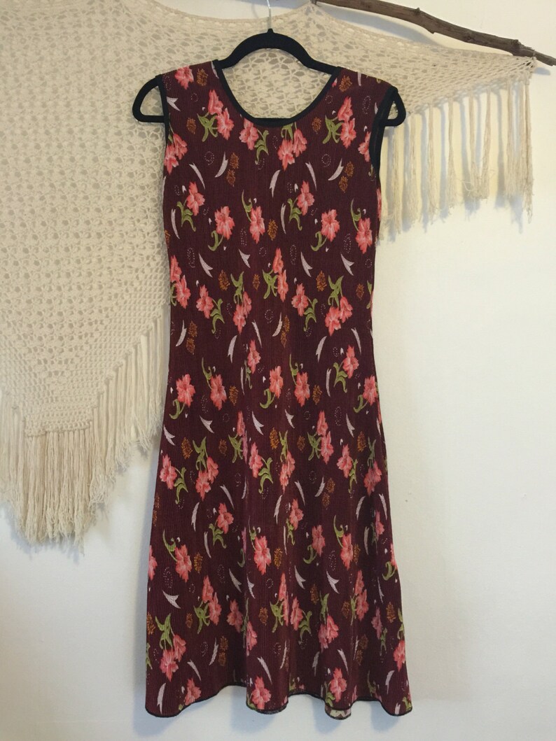 May include: A sleeveless burgundy dress with a floral print. The dress has a round neckline and a fitted bodice. The skirt is slightly flared and falls to the knees.
