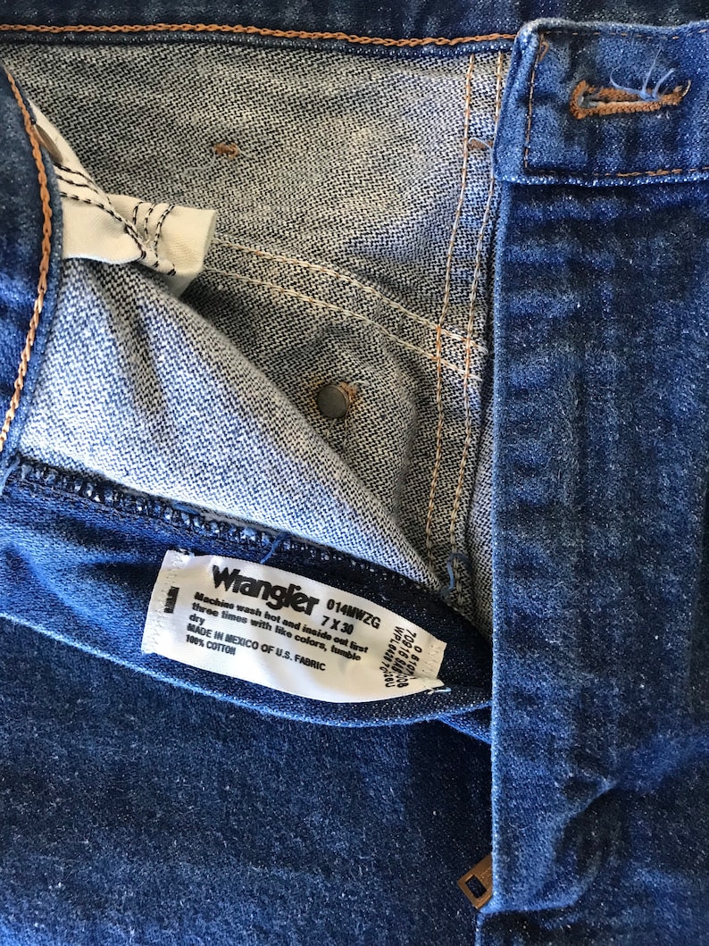 Może przedstawiać: Etykieta dżins&oacute;w Wrangler w kolorze niebieskim z białym tekstem, kt&oacute;ry brzmi "Wrangler 014MWZG 7X30 Machine wash hot and inside out first three times with like colors, tumble dry MADE IN MEXICO OF U.S. FABRIC 100% COTTON".