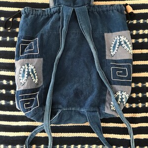 Puede incluir: Una mochila de lona azul con patrones geom&eacute;tricos y dise&ntilde;os de mariposas bordados. La mochila tiene correas ajustables.