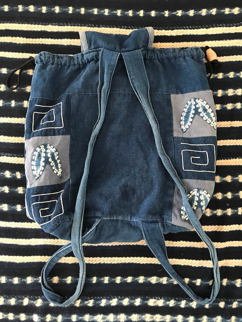 Puede incluir: Una mochila de lona azul con patrones geom&eacute;tricos y dise&ntilde;os de mariposas bordados. La mochila tiene correas ajustables.