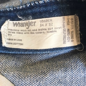 May include: A white tag with black text that reads "Wrangler 936DEN 34 x 32" and "Machine wash hot and inside out first three times with like colors, tumble dry" and "Made in USA 100% Cotton".