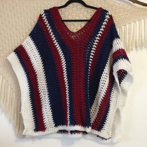 May include: A striped crochet poncho in white, red, and blue. The poncho has a V-neck and a loose fit.