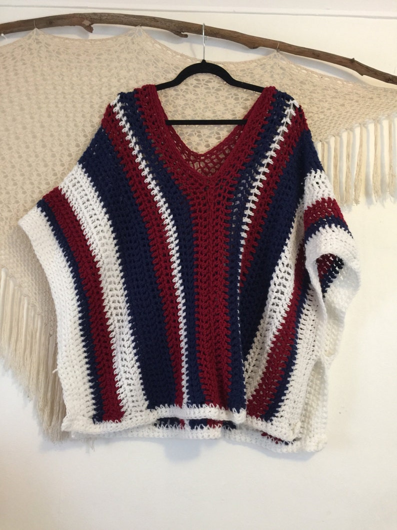May include: A striped crochet poncho in white, red, and blue. The poncho has a V-neck and a loose fit.