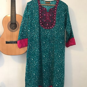 Puede incluir: Una t&uacute;nica azul turquesa con un cuello bordado en rosa y plata y un ribete rosa alrededor de las mangas y el dobladillo.