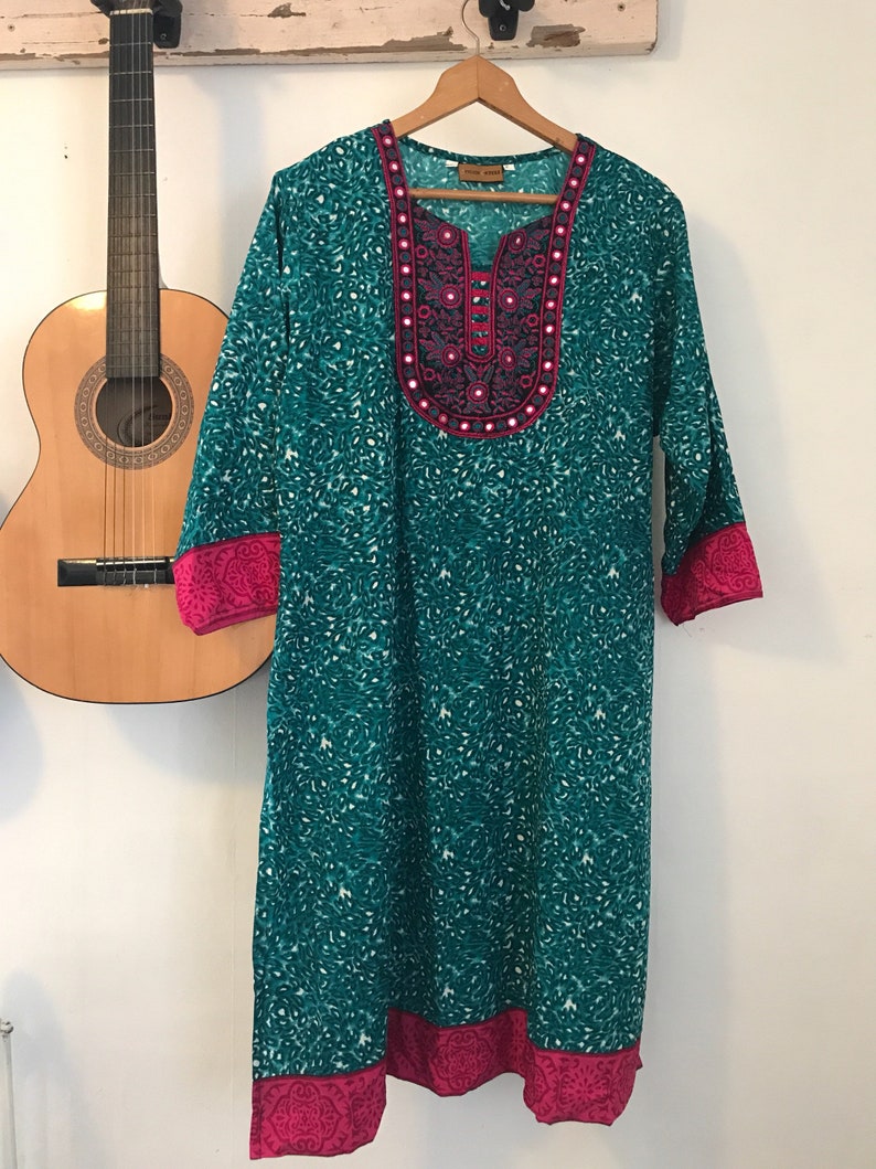 Puede incluir: Una t&uacute;nica azul turquesa con un cuello bordado en rosa y plata y un ribete rosa alrededor de las mangas y el dobladillo.