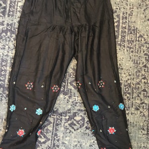 May include: Black pants with embroidered floral details in shades of blue, red, and white.