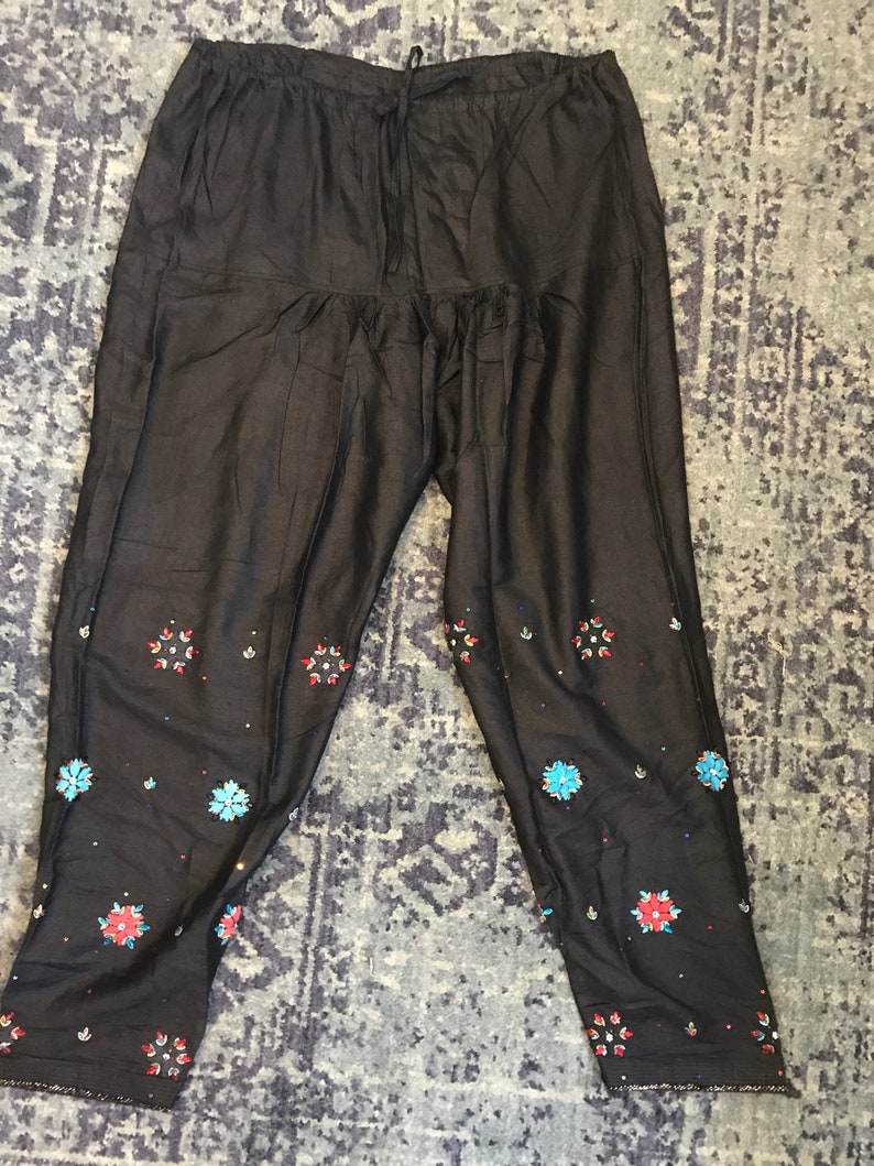 May include: Black pants with embroidered floral details in shades of blue, red, and white.