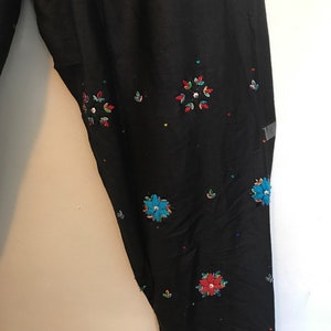 May include: Black pants with colorful embroidered flowers and sequins.