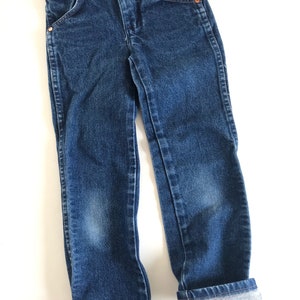 May include: Blue denim jeans with copper rivets and pockets. The jeans have a classic five-pocket design and are cuffed at the ankles. The jeans are made of a durable denim fabric and are suitable for everyday wear.