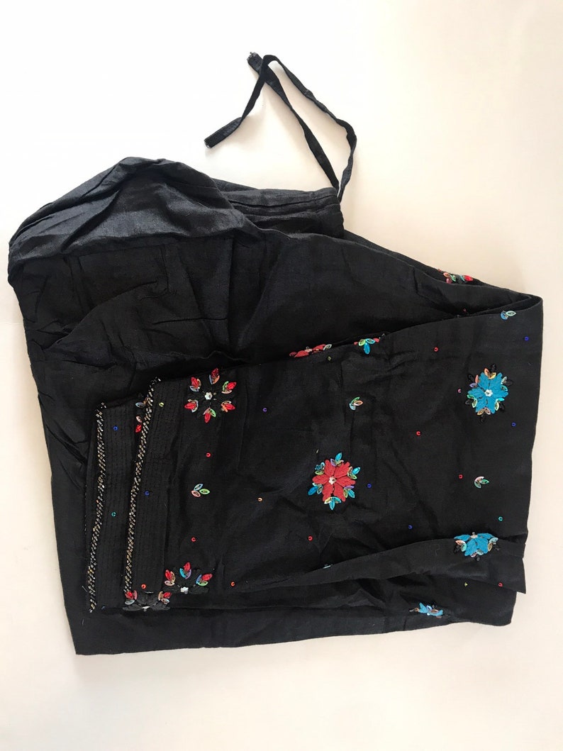 May include: Black cotton pants with a drawstring waist and embroidered floral designs in red, blue, and green.