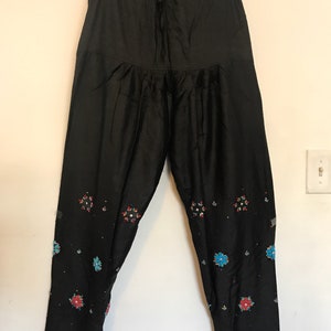 May include: Black pants with a drawstring waist and embroidered floral designs in shades of blue, red, and white.