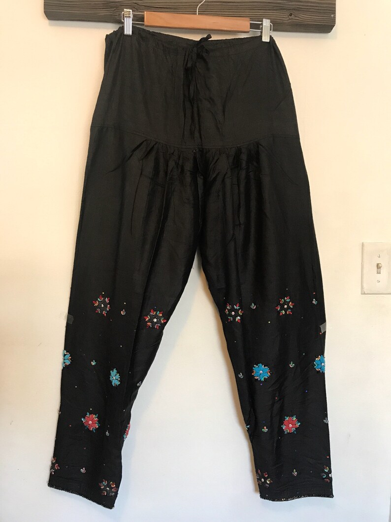 May include: Black pants with a drawstring waist and embroidered floral designs in shades of blue, red, and white.