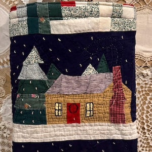 May include: A quilted tote bag featuring a winter scene with a house, trees, and falling snow. The bag has a beige handle and is made of various fabric patches in shades of blue, green, red, and beige. The house has a red door and a plaid chimney.