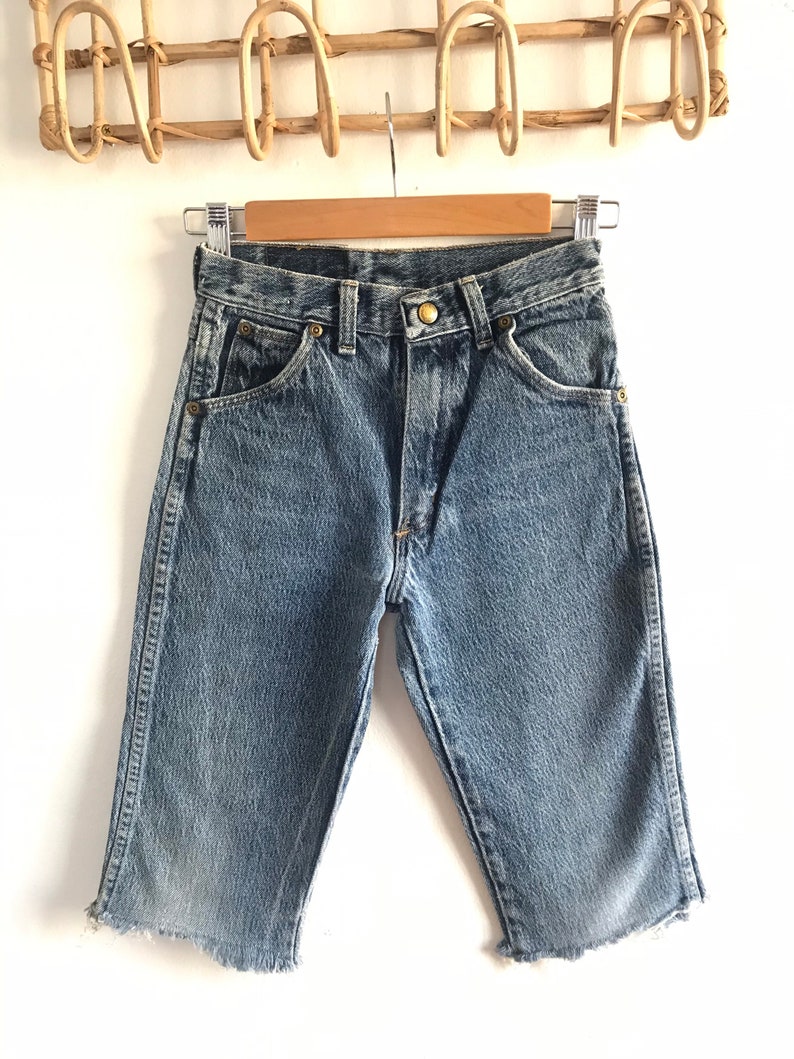 May include: A pair of light blue denim shorts with a frayed hem. The shorts have a classic five-pocket design and a button fly.