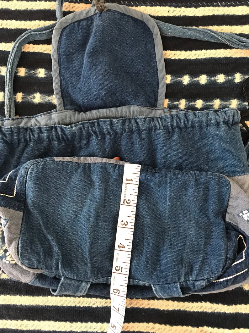 Puede incluir: Una bolsa de cord&oacute;n de mezclilla azul con un bolsillo de solapa y una cinta m&eacute;trica. La bolsa est&aacute; hecha de mezclilla de retazos y tiene un cierre de cord&oacute;n.