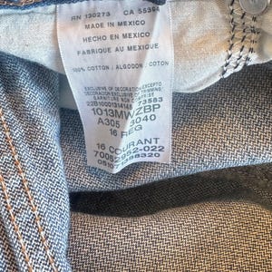 May include: Blue denim jeans featuring an internal white fabric care label with black text including RN 130273, CA 55394, Made in Mexico, 100% cotton, and size 16 REG. The jeans include a dark blue elastic waistband adjuster and a black button.