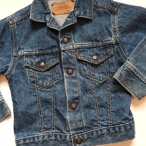 K&ouml;nnte beinhalten: Eine blaue Vintage-Jeansjacke mit einem braunen Leder-Levi's-Etikett und kupferfarbenen Kn&ouml;pfen.