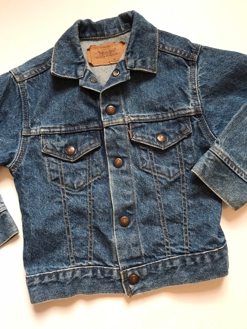 K&ouml;nnte beinhalten: Eine blaue Vintage-Jeansjacke mit einem braunen Leder-Levi's-Etikett und kupferfarbenen Kn&ouml;pfen.