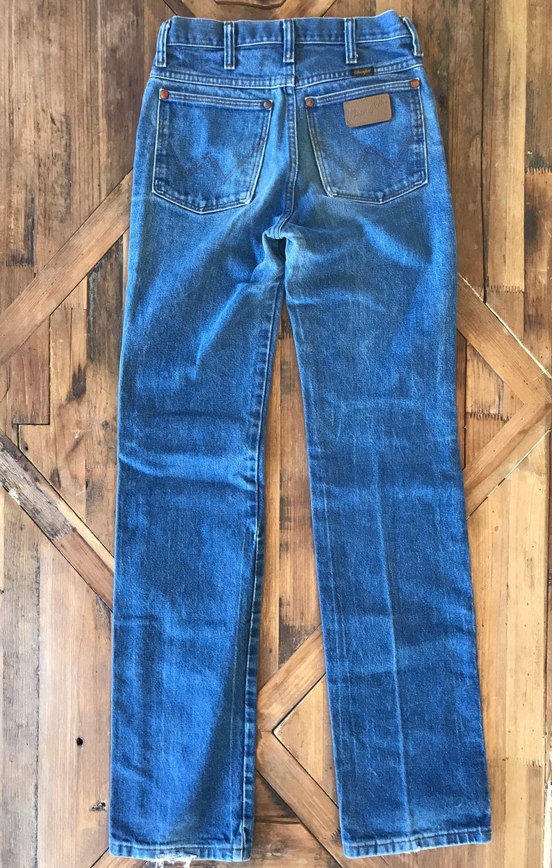 May include: A pair of blue denim jeans with a brown leather patch on the back pocket that says "Wrangler".