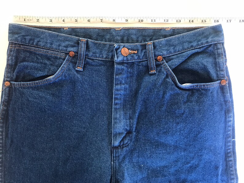 May include: A pair of blue denim jeans with a copper button and rivets. The jeans have two front pockets and two back pockets.