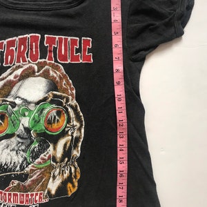 May include: Black t-shirt with a red "Jethro Tull" graphic and a cartoon illustration of a man wearing goggles. The text "Stormwatch... Tour '80" is printed below the illustration.