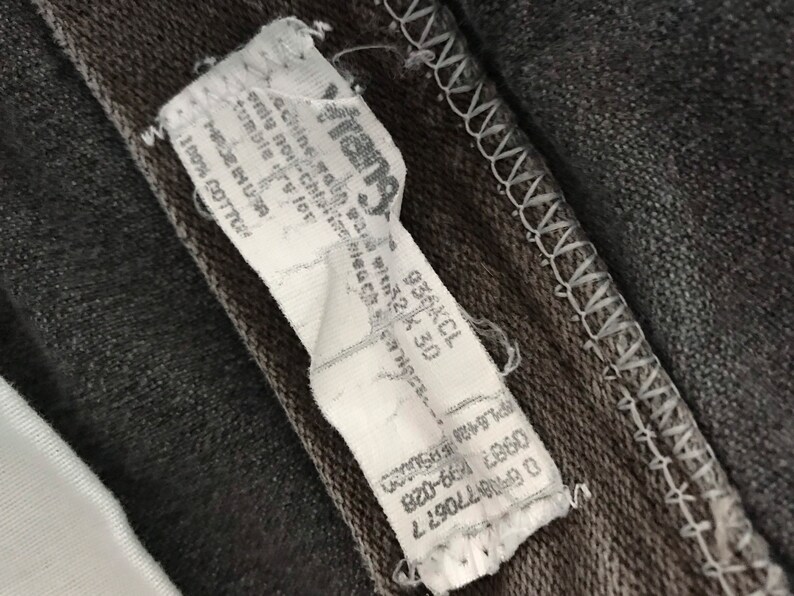 May include: A white tag with black text attached to a dark gray fabric. The tag reads "Frang", "Machine wash cold", "Tumble dry low", "Made in USA", "100% Cotton", "PL642 EPSUCCO", "0987 1899-028", "08770677", and "936KCL 230".