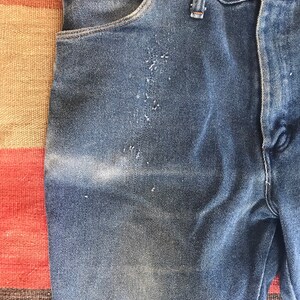May include: A pair of blue denim jeans with a faded look and a light brown belt loop. The jeans have a front pocket and a back pocket.