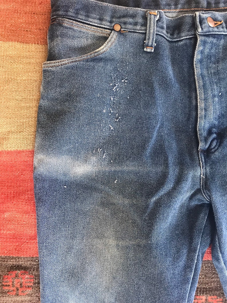 May include: A pair of blue denim jeans with a faded look and a light brown belt loop. The jeans have a front pocket and a back pocket.