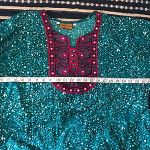 Puede incluir: Una t&uacute;nica azul turquesa con un cuello bordado en rosa y negro. El cuello tiene forma de V con una peque&ntilde;a abertura en la parte superior. La t&uacute;nica tiene un estampado de leopardo blanco y turquesa.