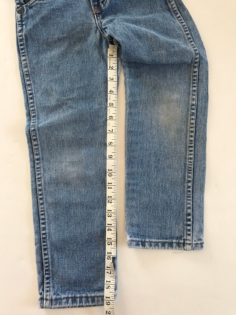 May include: A pair of light blue denim jeans with a seam down the outside of each leg. The jeans are measured with a tape measure, showing a length of 19 inches.