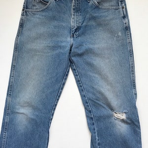 Pu&ograve; includere: Un paio di jeans in denim blu chiaro con un piccolo buco sul ginocchio destro.